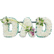 The photograph presents a dignified funeral tribute that spells out DAD in large, upright letters, composed entirely of white flowers and framed with green detail. Each letter is three-dimensional and generously filled with tightly clustered white chrysanthemums, their rounded petals overlapping to form a soft, cushion-like surface that appears comforting to the touch. Around the outer edges of the letters runs a continuous band of rich emerald green ribbon, artfully ruffled to add texture, definition, and a fresh contrast to the snowy blooms. Behind the tribute, a dark supporting frame with horizontal bars can just be glimpsed, indicating that the piece is mounted on a stand, as it would be when displayed at a funeral or memorial service in Oxford. On the upper left curve of the first D sits a small, elegant spray of white freesias and lush foliage, their slender stems and buds gently resting on the chrysanthemum base. Two long, graceful green stems then sweep from this point across towards the central A, drawing the eye to a striking focal arrangement. At their meeting point, nestled at the base and lower side of the A, two deep purple calla lilies unfurl their trumpet-shaped blooms among a cluster of white flowers and glossy green leaves, adding a rich, solemn accent of colour. The final D on the right is finished with a smaller coordinating cluster of white blooms and greenery on its upper right side, mirroring the first letter and creating balance. The overall effect is one of quiet love, respect, and remembrance, a personal floral message many Oxford families might choose when saying a last goodbye to a cherished dad.