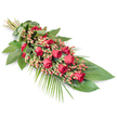An elegantly crafted sympathy spray lies diagonally across a pure white background, its refined shape and rich colours creating a sense of quiet, solemn beauty. At the top left, the stems are gathered neatly together and wrapped in a wide band of glossy green leaf, giving the impression of a carefully hand-tied sheaf ready to be carried into a funeral or memorial service somewhere in Oxford. From this gathered point, the flowers fan out, forming a long, tapering form that narrows towards the lower right, like a gentle green and red arc. Deep red roses dominate the centre of the composition; their velvety petals range from tightly closed buds to blooms that are softly unfurling and a few that are more fully open, offering a sense of tender progression and depth. Between the roses, clusters of small Hypericum berries in pinkish-red and soft coral hues add delicate texture and subtle highlights, their rounded shapes contrasting with the layered rose petals. Surrounding this core of flowers, lush foliage creates a strong, supportive base. Large, dark green leaves overlap to form a dense, polished backdrop, while lighter, feathery palm fronds and slender stems arch outward, lending a sense of movement and grace, as though stirred by a light breeze through one of Oxford's quiet churchyards. Every element is thoughtfully placed, with the interplay of rich reds and deep greens conveying tradition, love, and respect. This funeral spray feels especially suited to offering condolences or a final farewell at a service, cremation, or graveside ceremony within the local Oxford community.