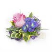 A compact, exquisitely crafted floral corsage or boutonnière laid on a clean white backdrop, described as if held in the light outside Oxford's Botanic Garden on a soft spring morning. At its centre sits a single, partially opened rose whose inner petals melt from a pale lavender-pink to a vivid fuchsia at the outer edges, the velvety layers catching light and suggesting a gentle, sweet scent. Nestled immediately to the right is a cluster of intensely indigo-purple florets-hydrangea-like in texture-with each tiny bloom punctuated by a bright blue and lime-yellow-green centre that offers a jewel-like contrast against the rose. Surrounding the flowers, a mix of greenery creates depth and movement: broad variegated ivy leaves with deep emerald cores and sunny golden-yellow margins frame the bouquet; slender, silvery-green foliage, reminiscent of lavender leaves, softens the silhouette; and a sculptural striped green-and-cream leaf curls elegantly to add modern geometry. Wispy, asparagus-fern-like sprigs feather through the composition, lending airiness and a tactile, almost ticklish softness. The arrangement is anchored on an intricate web of dark purple mesh that peeks from beneath, adding shadow, texture and a contemporary shimmer. Along the lower right, a short strand of lustrous white pearls is visible, suggesting a wristlet or decorative pin that nods to traditional formality. Perfect for a college ball, May Day celebration, or a wedding pinned to a lapel in Jericho or the High, this piece balances romantic bloom and refined detail, the work of a careful florist mindful of texture, proportion and the quiet joy of being worn.