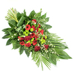 An elongated floral sympathy spray is captured here on a simple white background, its graceful, tapering form evoking the traditional shape of a funeral or casket arrangement. The design begins with a full, rounded cluster of flowers and then narrows elegantly to a soft point, giving a sense of direction and flow, as though gently guiding the eye along a final farewell. Deep red tones command attention in the central section: velvety roses unfurling at different stages, bold gerbera daisies marked by darker central discs, and clusters of ruffled red carnations that bring richness and texture. Interwoven with these are bright apple- and lime-green button chrysanthemums, small and spherical, their vivid colour offering a fresh, modern counterpoint to the solemn reds, much like seeing new foliage along the paths of South Park in Oxford. Tiny white filler flowers, perhaps dainty daisies or bell-like blooms, weave lightly through the spray, softening edges and adding a gentle brightness. The flowers sit within a generous bed of mixed greenery, including glossy broad leaves such as salal or ruscus, feathery ferns, and slender palm fronds that stretch outward, particularly noticeable towards the lower right, where they form a sweeping, fan-like accent. At the upper left, a structured bundle of tall green stems or leaves rises in a neat cluster, its base artistically wrapped with a single broad leaf, adding a contemporary, sculptural note. This thoughtfully balanced tribute, created with the sensitivity of an Oxford florist who understands the atmosphere of local services and crematoria, feels quietly dignified and is visually suited to moments of remembrance and condolence.