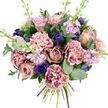 Set against a clean white background, this hand-tied bouquet appears almost to float, its colours and forms carefully composed like an elegant Oxford still life. At the centre, several generous garden roses bloom in shades of blush pink, dusty mauve, and antique rose, their gently curling petals layered so densely that they form soft, rounded hearts of colour. Around them, ruffled carnations add both volume and intricate texture, their bi-colour petals moving from creamy, almost porcelain centres to edges tinted with blush, rose, and plum-pink, giving each flower a delicate, vintage charm. To offset these warm tones, the florist has woven in deep indigo and royal blue blooms-some closed in sleek, bud-like shapes, others open as dramatic anemones with near-black centres that create a strong visual anchor. Slim stems of lilac and pale lavender stock rise between the larger flowers, each stem dotted with many petite blossoms that lend an airy, vertical lift, reminiscent of cottage borders in North Oxford gardens. The bouquet is framed with a mix of lush green foliage: dark, glossy leaves that cradle the flowers, and rounded, silvery eucalyptus that adds a cool, misty green note and a hint of clean, herbal scent. The stems are visibly tied at the base, underscoring the hand-crafted nature of a fresh flower delivery making its way across Oxford, from Littlemore to Jericho. Overall, the arrangement feels soothing and romantic, ideal for expressing affection, celebrating a birthday, or sending comfort to someone who needs a gentle reminder of beauty and care.