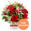 A rich and romantic bouquet is captured here, floating against a clean white background so that every flower and leaf can be appreciated. At its core are plush red roses, some still in tight buds with petals spiralling inward, others more open and revealing their intricate layers, all suggesting freshness and heartfelt emotion. Interlaced with the roses are smaller, deep red blossoms that resemble alstroemeria or similar multi-petalled flowers, adding sculptural interest and reinforcing the passionate colour story. Among these deeper tones, feathery sprays of tiny pale pink and white filler flowers-waxflower-like in their dainty clusters-provide a soft, almost cloud-like lightness. Encircling the blooms is an abundance of greenery that builds the arrangement into a full, rounded dome: smooth, glossy leaves sit alongside more delicate, textured sprigs, giving the bouquet a lively, garden-inspired feel. Rich burgundy and reddish-brown leaves with gentle veining are tucked between the greens, bringing drama, depth, and an elegant contrast reminiscent of autumn walks through University Parks in Oxford. The stems are arranged in a sleek, clear glass vase with a rectangular base, the transparent sides showcasing the neat green stems and clean water, lending a modern, polished look suitable for any home or office. A charming red ribbon patterned with small white hearts is tied around the vase, quietly reinforcing the romantic intent-perfect for a surprise delivery to a loved one in central Oxford or along the leafy streets of Summertown. In the bottom right corner, a bright orange circular label with bold white uppercase lettering clearly states VASE INCLUDED, indicating that this floral gift arrives ready to place and enjoy.