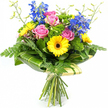 Against a bright white background, a vibrant mixed bouquet appears crisp and full of life, as though just finished by a local Oxford florist preparing for a delivery run through Jericho and the city centre. At its heart are several pink roses, their petals opening in gentle spirals with a velvety texture that suggests softness to the touch and a subtle, classic fragrance. Surrounding these are sunny yellow gerbera daisies, each one featuring a distinctive dark brown centre that anchors the eye and adds depth to the cheerful colour palette. Rising above and between the rounder blooms, tall blue delphinium stems create vertical lines and a cool, elegant contrast, their many small florets giving the arrangement a slightly whimsical, meadow-like feel. A generous mix of greenery supports and frames the flowers: airy fern fronds trail lightly from the sides, glossy dark green leaves provide a structured backdrop, and clumps of brighter green, textured filler foliage tuck into any gaps, ensuring the bouquet looks full from every angle. Thin, pale green stems tipped with unopened buds stretch upwards here and there, adding a sense of movement and fresh growth. Around the lower half of the bouquet, broad tropical-style leaves-some subtly streaked with lighter green-curve gracefully to create a neat collar that transitions into a soft cream or pale green wrapping. This wrap gathers the long stems together, secured with a simple tie that hints at the cool weight of the flowers when held in hand. The bouquet feels happy and uplifting, perfect for sending congratulations to someone near the Oxford colleges, brightening a home in Summertown, or marking any everyday moment that deserves a splash of colour and care.